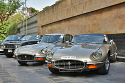 Two pristine examples of Jaguar E-Types – a coupe and a convertible. Both powered by V12s. An Aston Martin DBS lurking in the background. 
